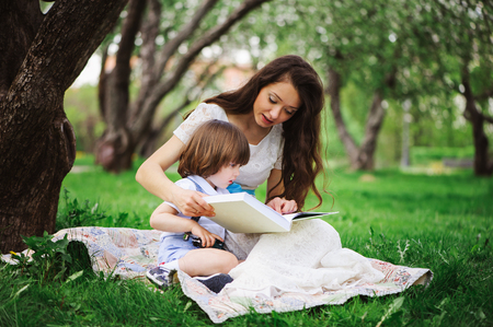 loving mother reading book to toddler son outdoor on picnic in spring or summer park. Happy family and mothers day conceptの写真素材