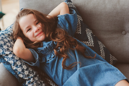 cute happy 5 years old child girl relaxing alone at home on cozy couchの写真素材