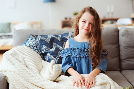 cute little child girl relaxing at home, sitting on couch, wrapped in cozy blanket. Kids health and seasonal flu healing conceptの写真素材