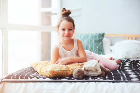 happy child girl wake up in the early morning in her room, lying on comfortable bed in cozy homely interiorの写真素材