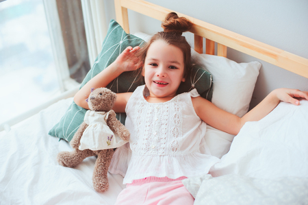 happy child girl wake up in the early morning in her room, lying on comfortable bed in cozy homely interiorの写真素材