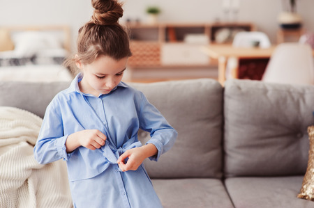 adorable happy 5 years old child girl checking bow on her fashion shirt at homeの写真素材