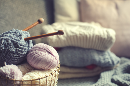 Grey and pink Yarn ball with knitting needles in metallic basket with knitted sweaters on background. Hobby, cozy homely weekend and hugge concept.の写真素材