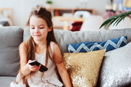 child girl watching tv at home on cozy couch. Modern scandinavian interior, kids and television conceptの写真素材