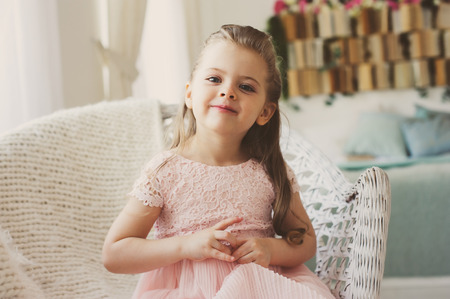 portrait of cute smiling 5 years old child girl sitting on chair at homeの写真素材