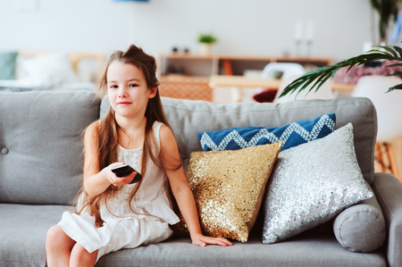 child girl watching tv at home on cozy couch. Modern scandinavian interior, kids and television conceptの写真素材