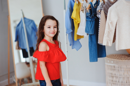 cute little child girl choosing new modern clothes in her wardrobe or store fitting room. Kid fashion and apparel storage concept.の写真素材