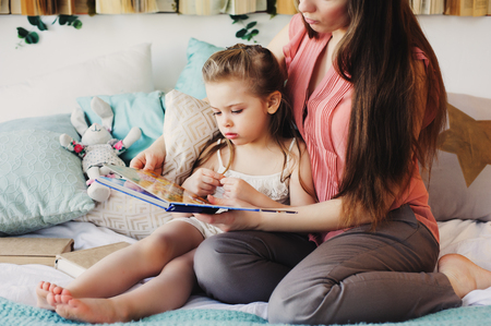 mother reading book to toddler daughter in bedroom for good night. Casual lifestyle capture of happy family at homeの写真素材