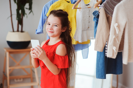 little child girl making selfie while trying on new clothes in her wardrobe or store fitting room. Kids fashion conceptの写真素材