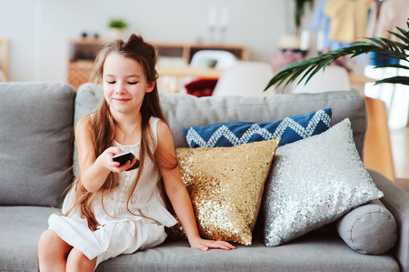 child girl watching tv at home on cozy couch. Modern scandinavian interior, kids and television conceptの写真素材