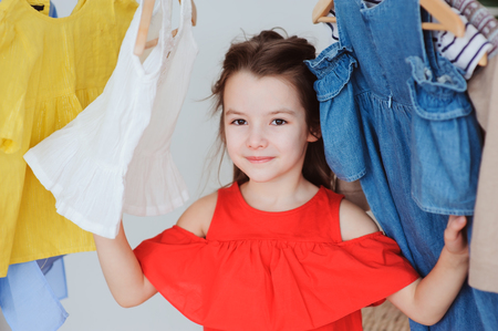cute little child girl choosing new modern clothes in her wardrobe or store fitting room. Kid fashion and apparel storage concept.の写真素材
