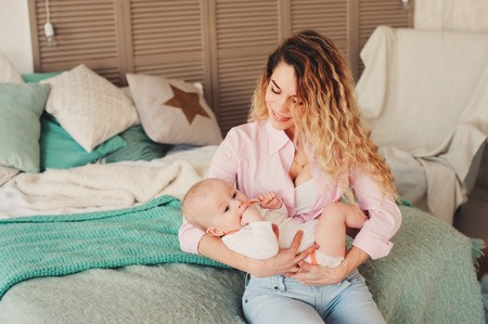 happy family at home. Mother holding baby son in bedroom in cozy weekend morningの写真素材