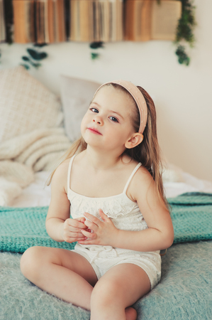 indoor portrait of sad 5 years old child girl sitting on bedの写真素材