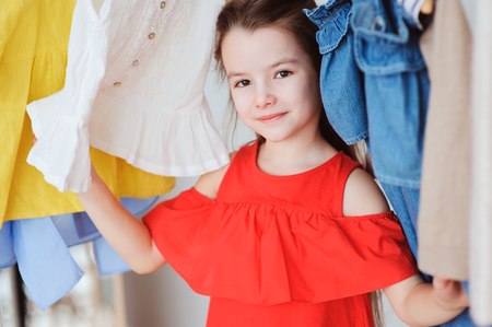 cute little child girl choosing new modern clothes in her wardrobe or store fitting room. Kid fashion and apparel storage concept.の写真素材