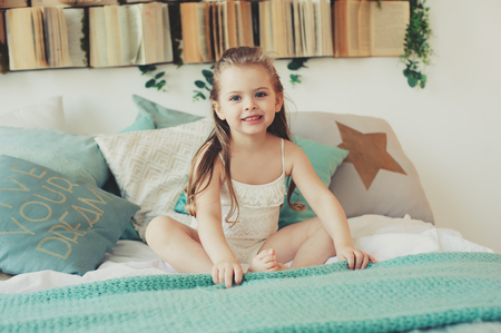 cute happy toddler girl sitting on bed in pajama. Child playing at home, casual lifestyle capture.の写真素材