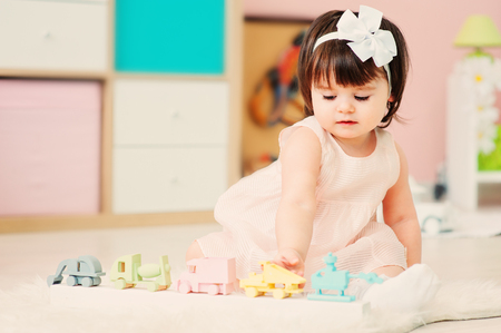cute happy 1 year old baby girl playing with wooden toys at home. Modern nursery interior, early learning conceptの写真素材
