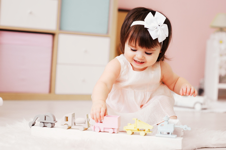 cute happy 1 year old baby girl playing with wooden toys at home. Modern nursery interior, early learning conceptの写真素材