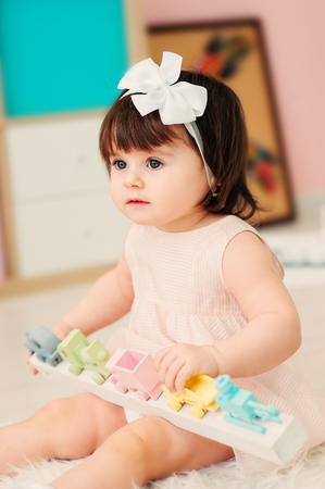 cute happy 1 year old baby girl playing with wooden toys at home. Modern nursery interior, early learning conceptの写真素材