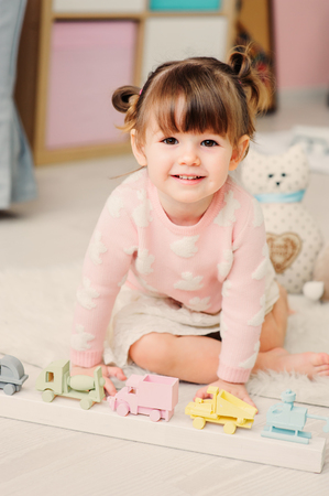 cute happy 2 years old baby girl playing with toys at home. Modern nursery interior in pastele tones, early learning conceptの写真素材