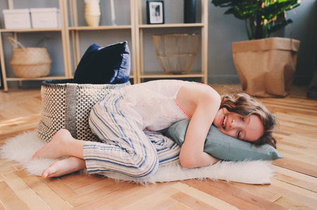 happy child girl having fun at home in lazy weekend morning, lying on the floor in pajamas and hug cozy pillowの写真素材