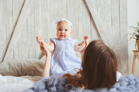happy mother and 9 month old baby in matching pajamas playing in bedroom in the morning. Cozy family weekend.の写真素材