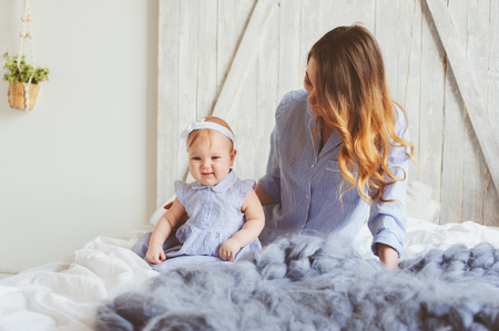 happy mother and 9 month old baby in matching pajamas playing in bedroom in the morning. Cozy family weekend.の写真素材