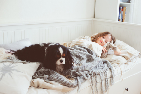 happy kid girl waking up in the morning in her bedroom with dog in bedの写真素材