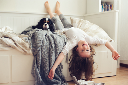happy kid girl waking up in the morning in her bedroom with dog in bedの写真素材