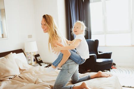 happy family playing at home. Mother and toddler daughter relaxing and having fun in bed in cozy...