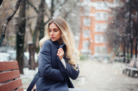 winter portrait of young woman walking on city streets in snowy day, wearing warm grey coatの写真素材
