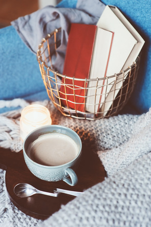 Cozy winter weekend at home. Morning with coffee or cocoa, books, warm knitted blanket and nordic style chair. Hygge concept.の写真素材