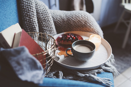 Cozy winter weekend at home. Morning with coffee or cocoa, books, warm knitted blanket and nordic style chair. Hygge concept.の写真素材
