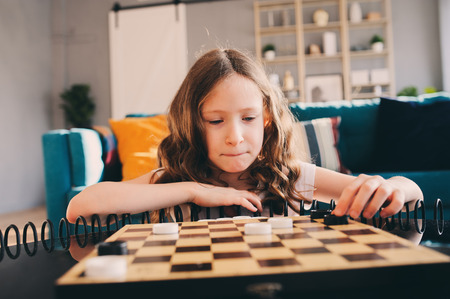 lifestyle shot of smart kid girl playing checkers at home. Board games for kids concept, candid series with real people in modern interiorの写真素材
