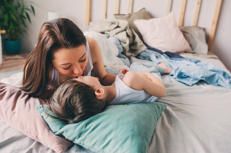 mother kisses her toddler son in bed for good night or good morning, casual lifestyle, happy family lifestyleの写真素材