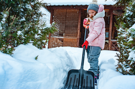 kid girl helping to clean pathway from snow with showel. Child playing in snowy winter gardenの写真素材