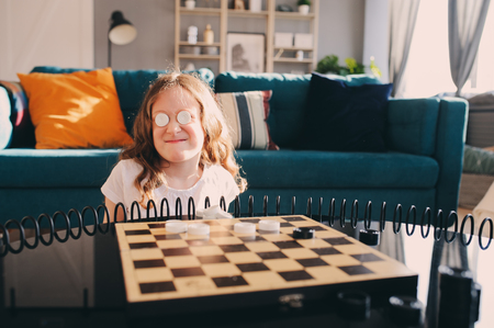 lifestyle shot of smart kid girl playing checkers at home. Board games for kids concept, candid series with real people in modern interiorの写真素材