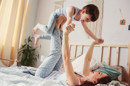 mother doing morning gymnastics with happy toddler son in bed. Happy family playing at homeの写真素材