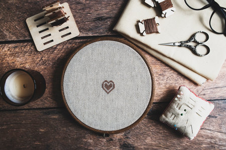cross stitch accessories. Linen cloth in hoop, scissors, cloth and floss on wooden background. indoor hobby concept.の写真素材