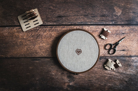 cross stitch accessories. Linen cloth in hoop, scissors, cloth and floss on wooden background. indoor hobby concept.の写真素材