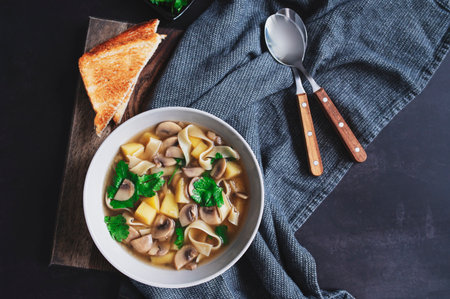 vegetarian noodle mushroom soup with potato served with toast on dark rustic backgroundの写真素材