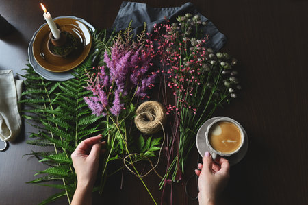 top view of florist woman hands making bouquet of summer garden flowers and ferns on rustic wooden tableの写真素材