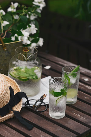 fresh lemonade with mint in summer garden. Blooming Philadelphus coronarius (Sweet Mock-orange, Jasmine) bouquet on wooden table with gardener tools. Summertime relaxの写真素材