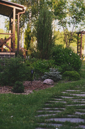 Beautiful summer garden view with curvy stone pathway and wooden archway (pergola). Natural rustic cottage garden with hostas, conifers and shrubsの写真素材