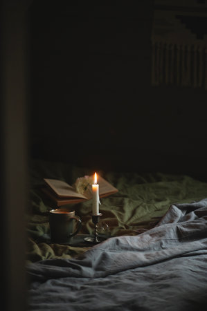 dark and moody cabin bedroom interior with green and gray bedlinen, coffee cup, book and candleの写真素材