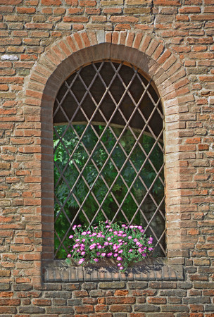old brick wall with a window with bars and flowersの写真素材