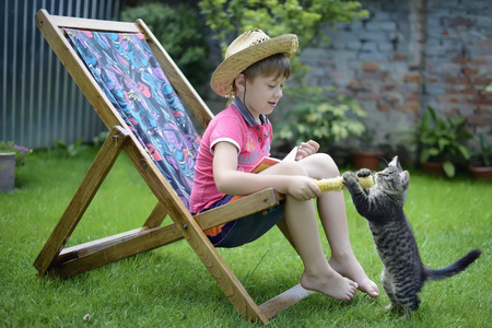 boy sitting on a lounge chair and playing with a catの写真素材