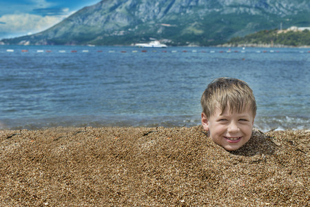 Boy buried in sand on the sea behind head smiling cloudy skyの写真素材