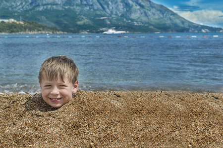 Boy buried in sand on the sea behind head smiling cloudy skyの写真素材