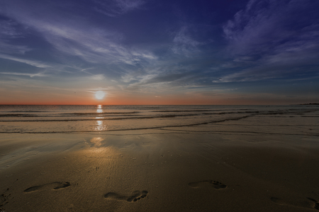 footprints in the sand waves in the sea coast sunsetの写真素材