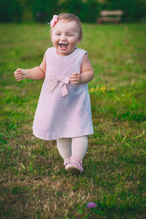 little pretty girl running through the grass and smiles, joy, mischief, childhoodの写真素材